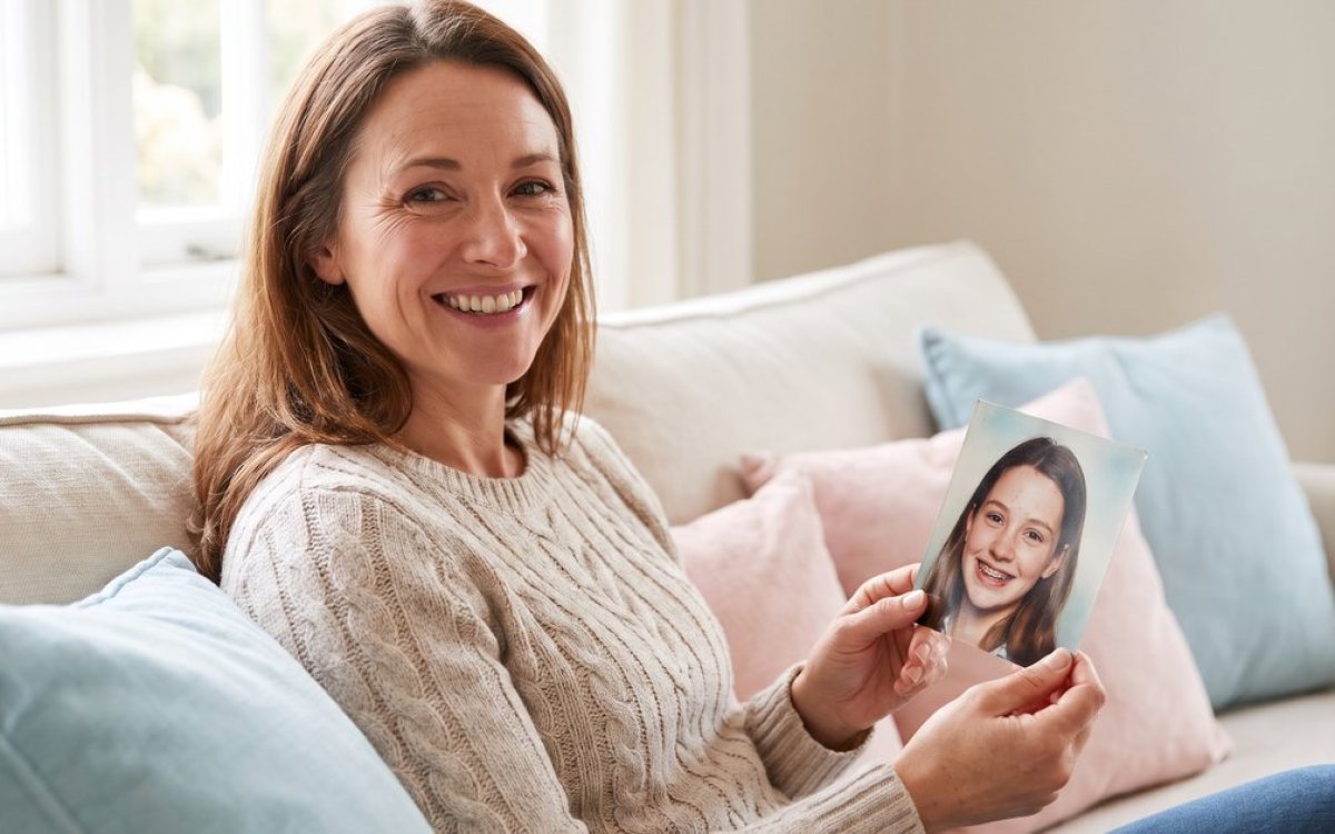 Frau hält lächelnd ein altes Foto, auf dem sie als Teenager eine Zahnspange trägt