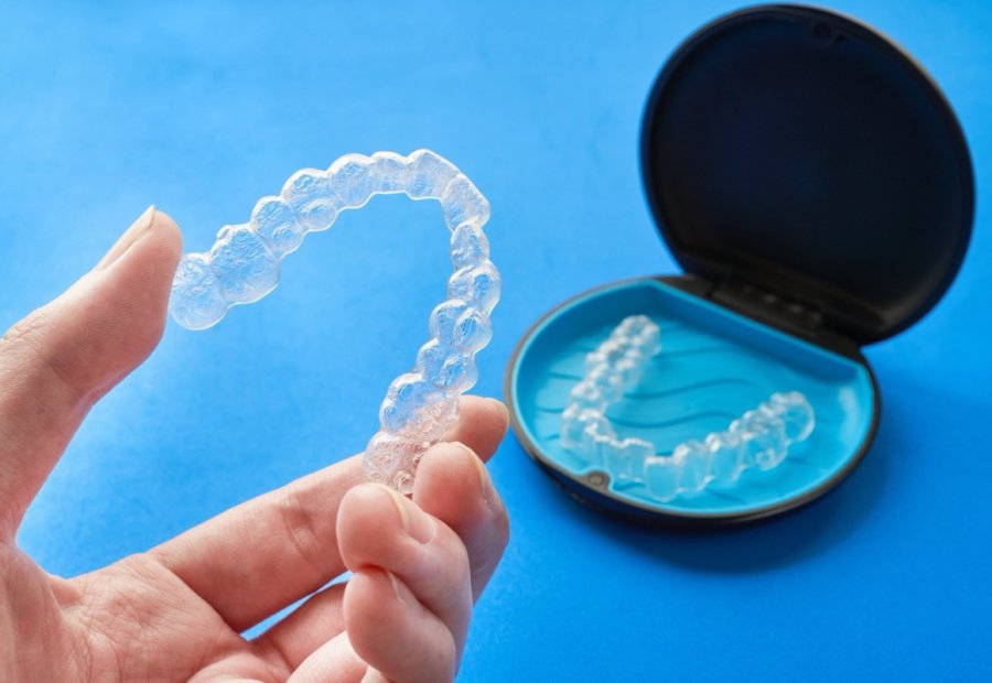 Clear aligner held in a hand next to an open aligner case
