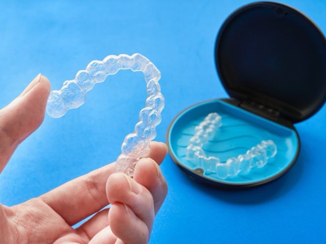 Transparente Zahnschiene in der Hand neben offener Schienenbox