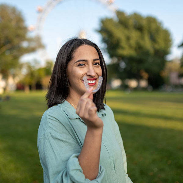 Sarah smiling in the park, holding a clear aligner