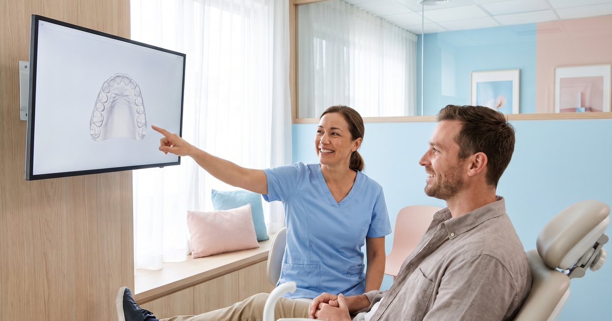Zahnärztin zeigt einem Patienten das 3D-Modell seiner Zähne am Bildschirm