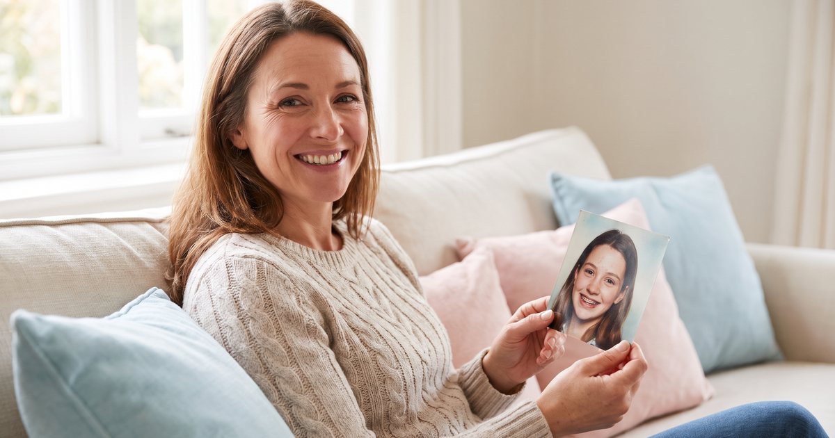 Frau hält lächelnd ein altes Foto, auf dem sie als Teenager eine Zahnspange trägt